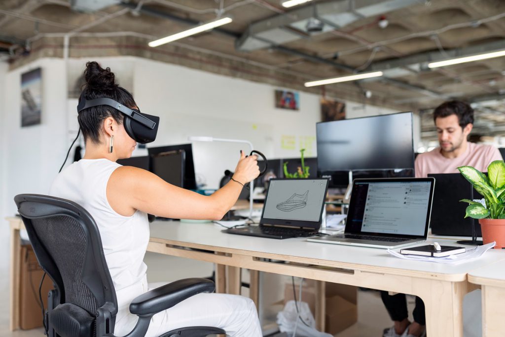 Frau mit Virtual Reality Brille sitzt am Schreibtisch und kreiert Design am Laptop