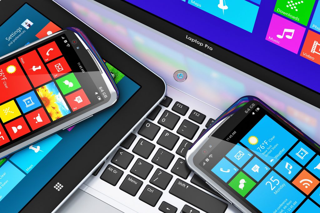 Verschiedene Endgeräte wie Smartphone, Tablet und Laptop liegen übereinander mit Apps auf den Bildschirmen