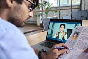 Indian human resource manager holding cv having virtual job interview conversation with remote female candidate during distant business video call on laptop computer. Online recruitment concept.
