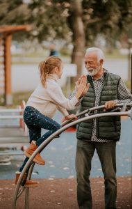 Handsome grandfather spending time with his granddaughter in park playground on autumn day